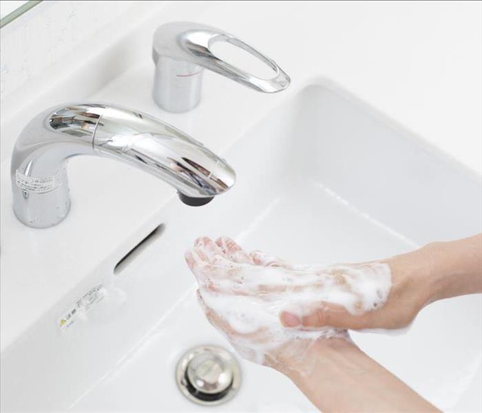 Hands of someone with soap washing them on a hands- free faucet