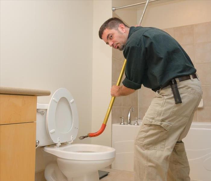 A plumber with a tool called "snake" trying to push out any blockage on a toilet